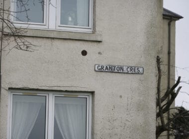 Article: Muirhouse, SLPs and the King of Fraud Image description: Close-up of a street sign reading “Granton Cres.” on a plain whitewashed building in Muirhouse, Edinburgh — the listed address for the shell company Octmedia involved in an international fraud investigation.