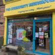 article headline: Ten years on, The Ferret is still digging — and looking ahead alt text: A bright yellow shopfront with blue trim in Govanhill, Glasgow, reading “The Community Newsroom” and “Everybody has a story… What’s yours?”. The window is decorated with a large hand-drawn cake and the words “Happy Birthday to The Ferret — 10 years of digging for facts!”, celebrating The Ferret’s 10th anniversary. Posters and flyers fill the other windows, and a small bench with plants sits outside.