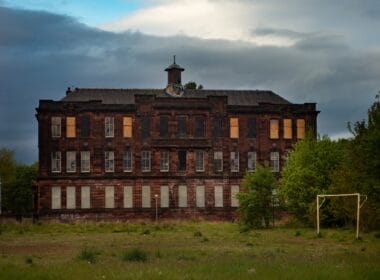 Article headline: Councils sell off 1,600 local assets amidst budget shortfalls Image description: A Derelict School Building With Boarded Up Windows And Overgrown Grounds in Glasgow, Scotland