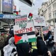 Article headline: Palestine Action: Why has the UK proscribed the group? Image description: People hold Palestinian flags and placards during a protest on a busy street in London’s West End, with theatre signs visible in the background.