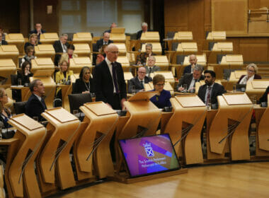 Deputy first minister John Swinney addresses the Scottish Parliament surrounded by MSPs.