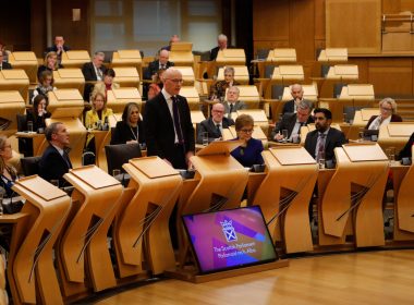 Deputy first minister John Swinney addresses the Scottish Parliament surrounded by MSPs.